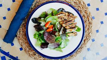 A plate of grilled chicken and salad on a woven mat.