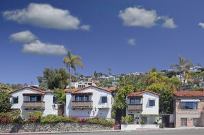 A row of white houses with red-tiled roofs, balconies, and a stone wall with plants in front. - Casa Laguna Hotel & Spa (Laguna Beach)