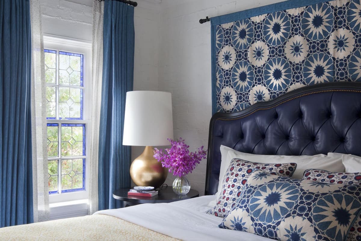 Quarto com uma cama grande, uma luminária decorativa em formato de estrela, uma janela com cortinas azuis e uma cabeceira estampada.