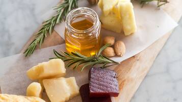 A wooden board with various cheeses, a jar of honey, almonds, and rosemary sprigs.