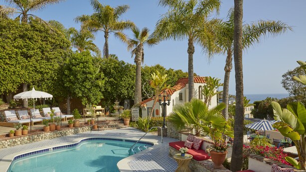 A pool area with lounge chairs, a stone wall, and palm trees. - Casa Laguna Hotel & Spa (Laguna Beach)