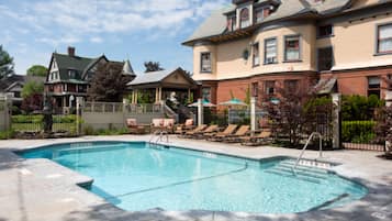 A swimming pool with lounge chairs and a covered area, surrounded by a brick building with multiple windows and a covered porch.