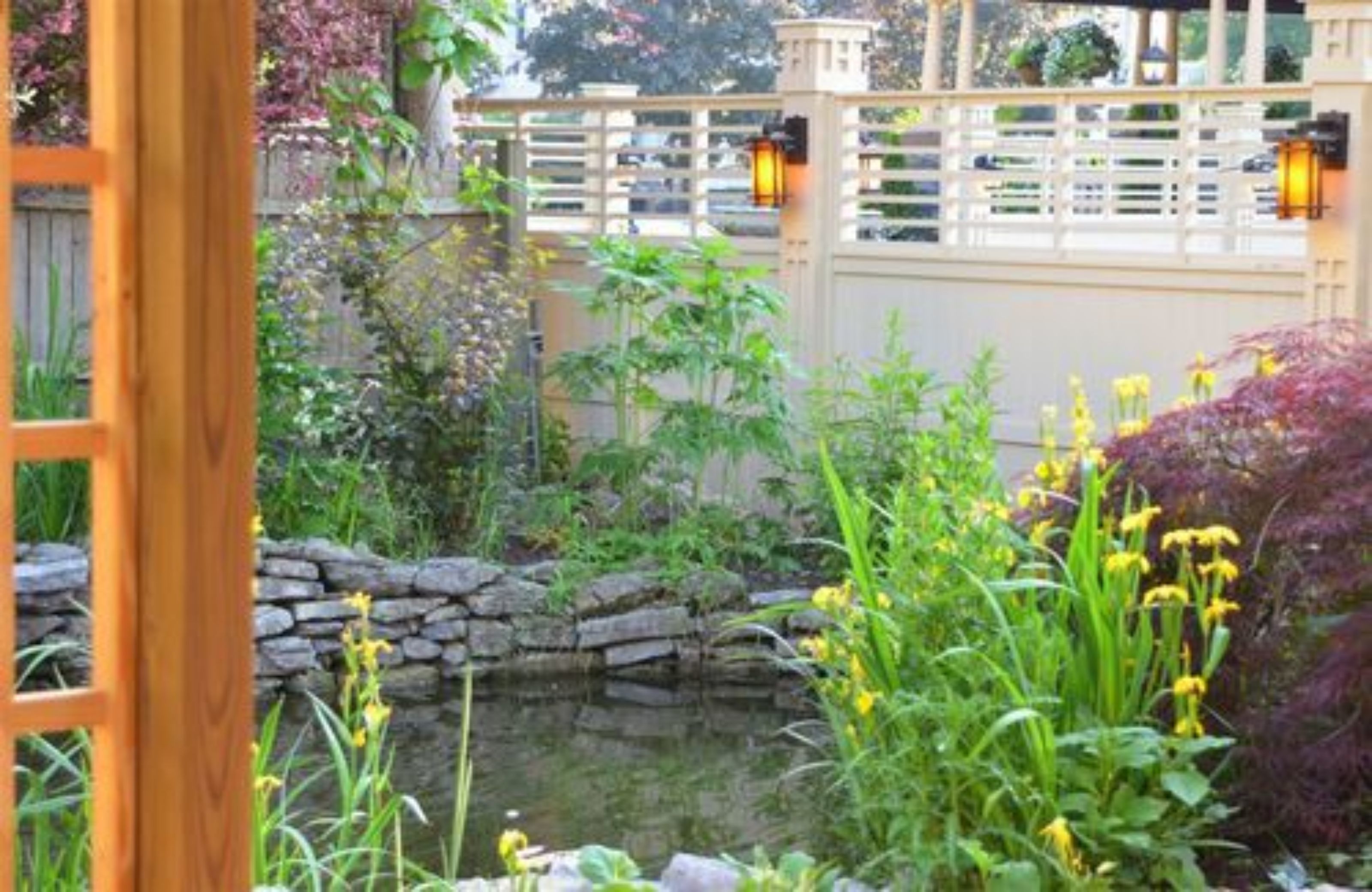 Un jardí amb un estany, una paret de pedra i una tanca de fusta.