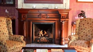 A room with a fireplace, two armchairs, and a table with books.