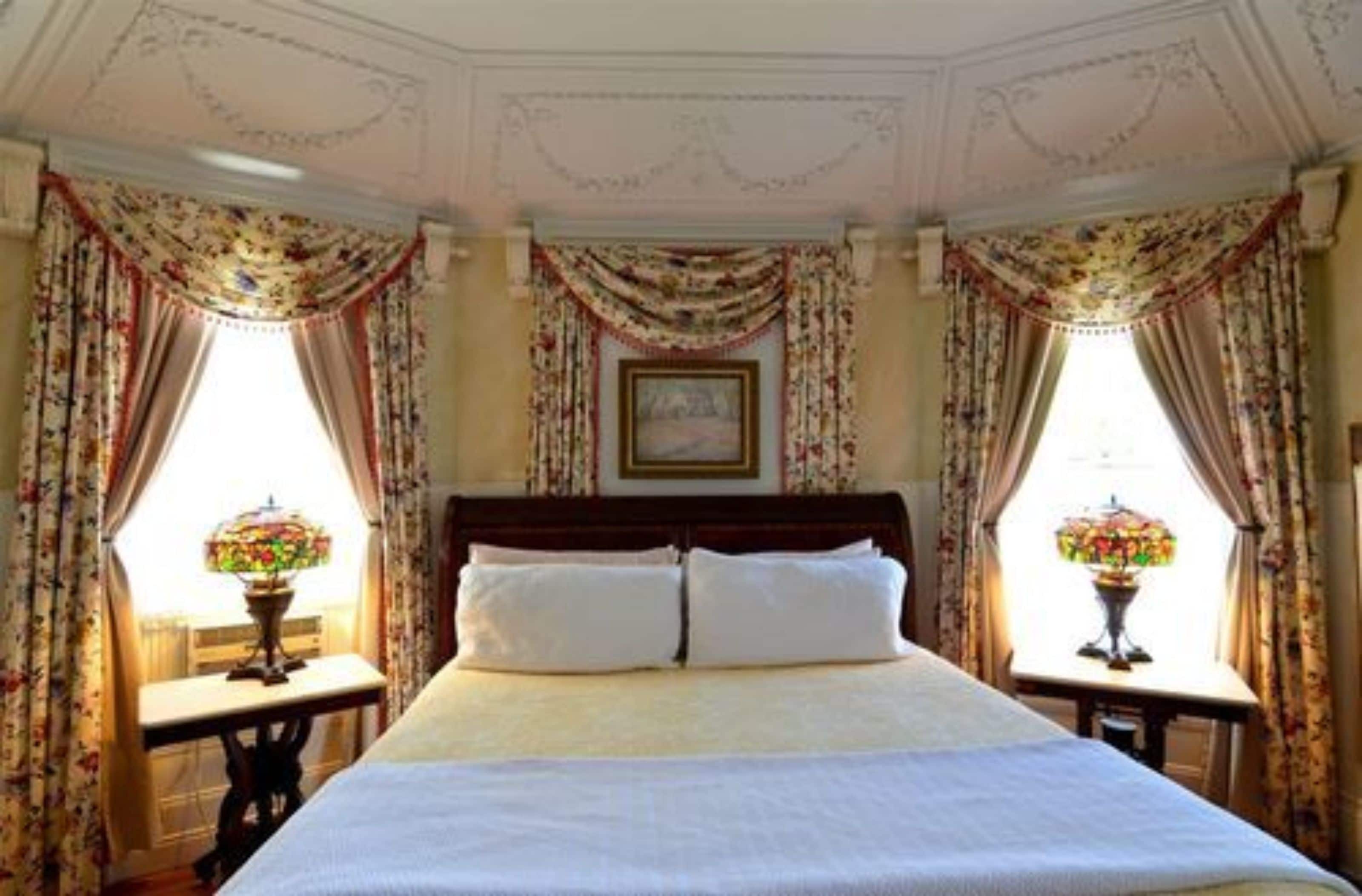 A bedroom with a large bed, floral curtains, and two table lamps.