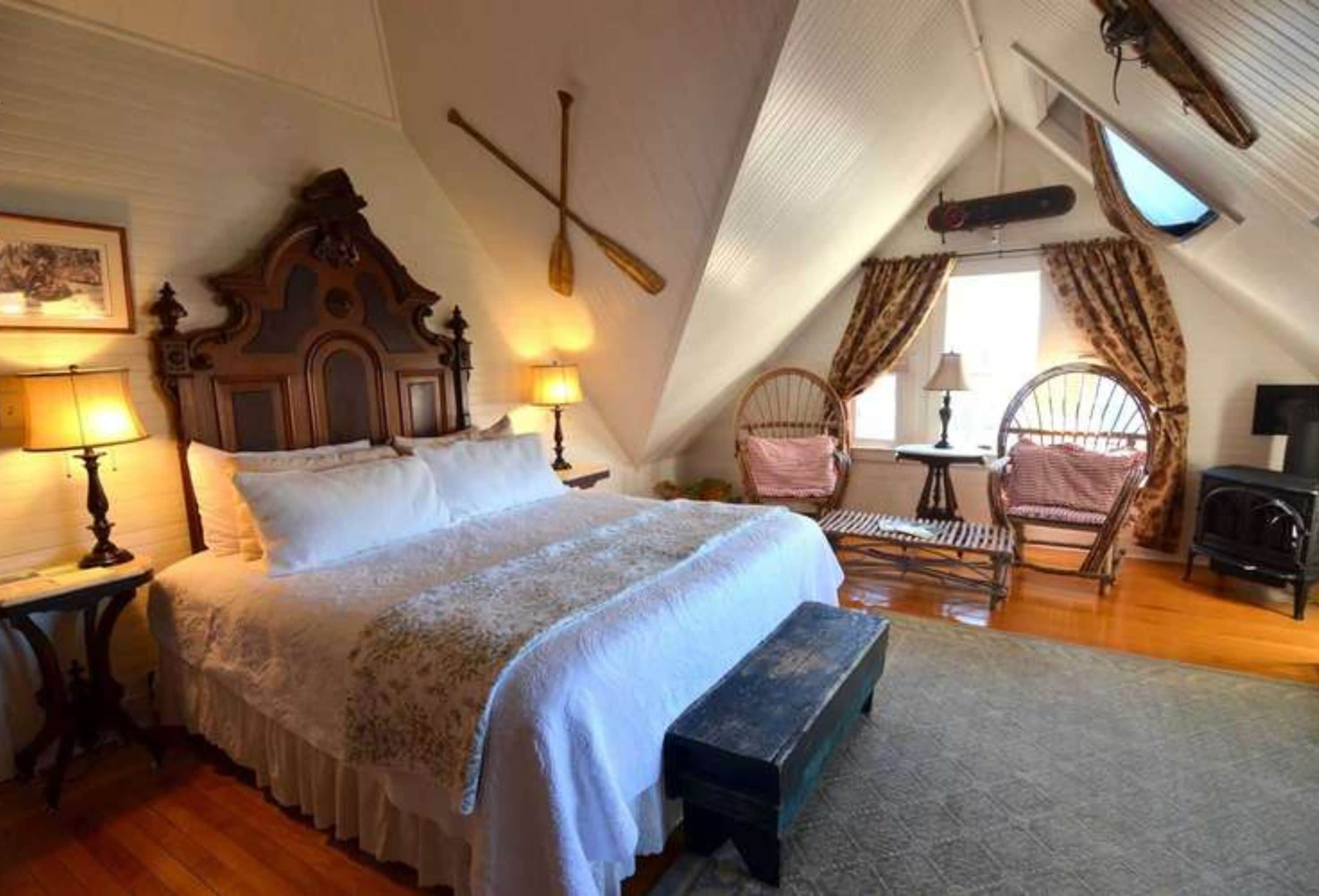 A cozy attic bedroom with a large bed, wooden headboard, and a rustic fireplace.