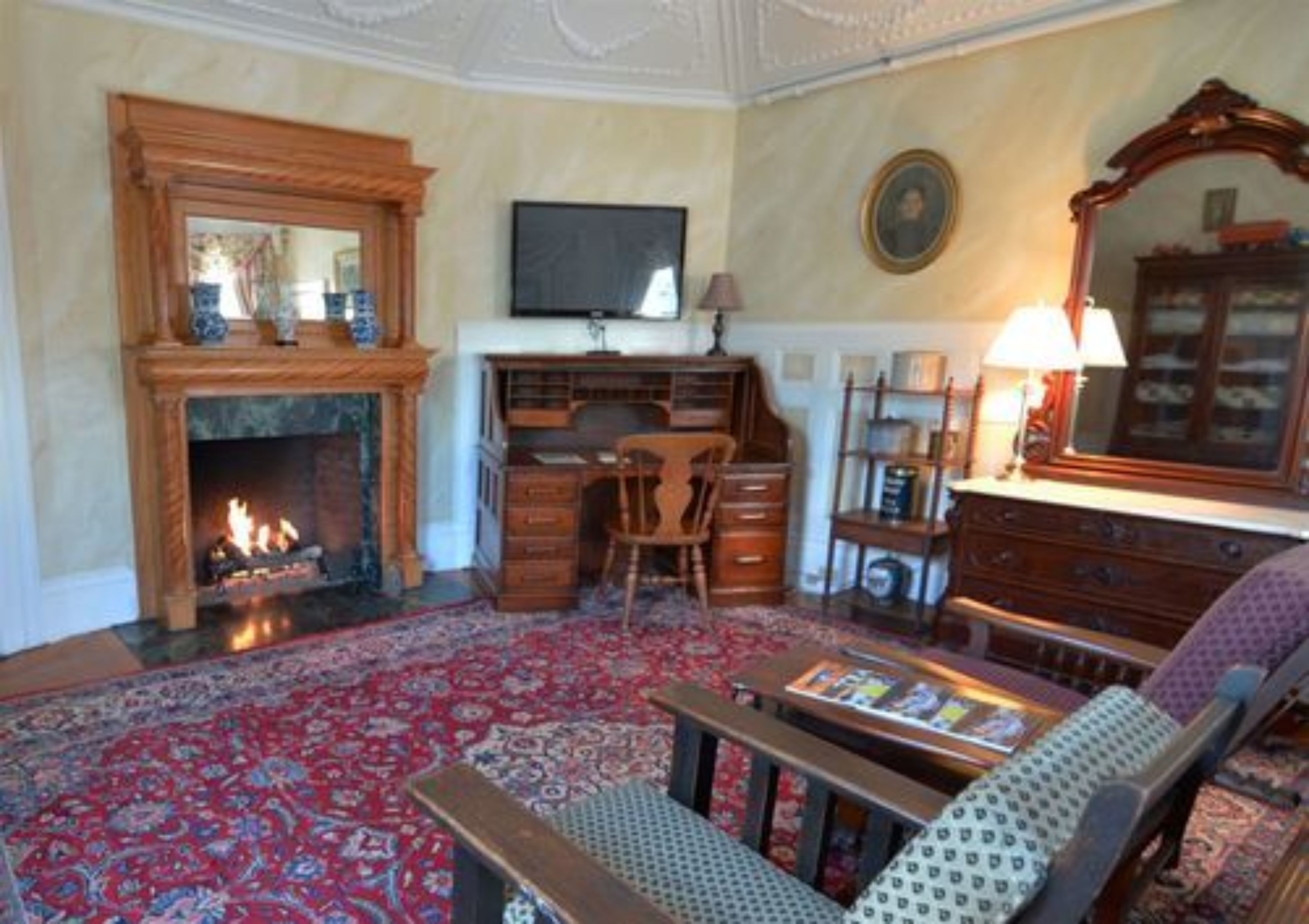 Una sala de estar con chimenea, un escritorio, un televisor y un espejo grande.