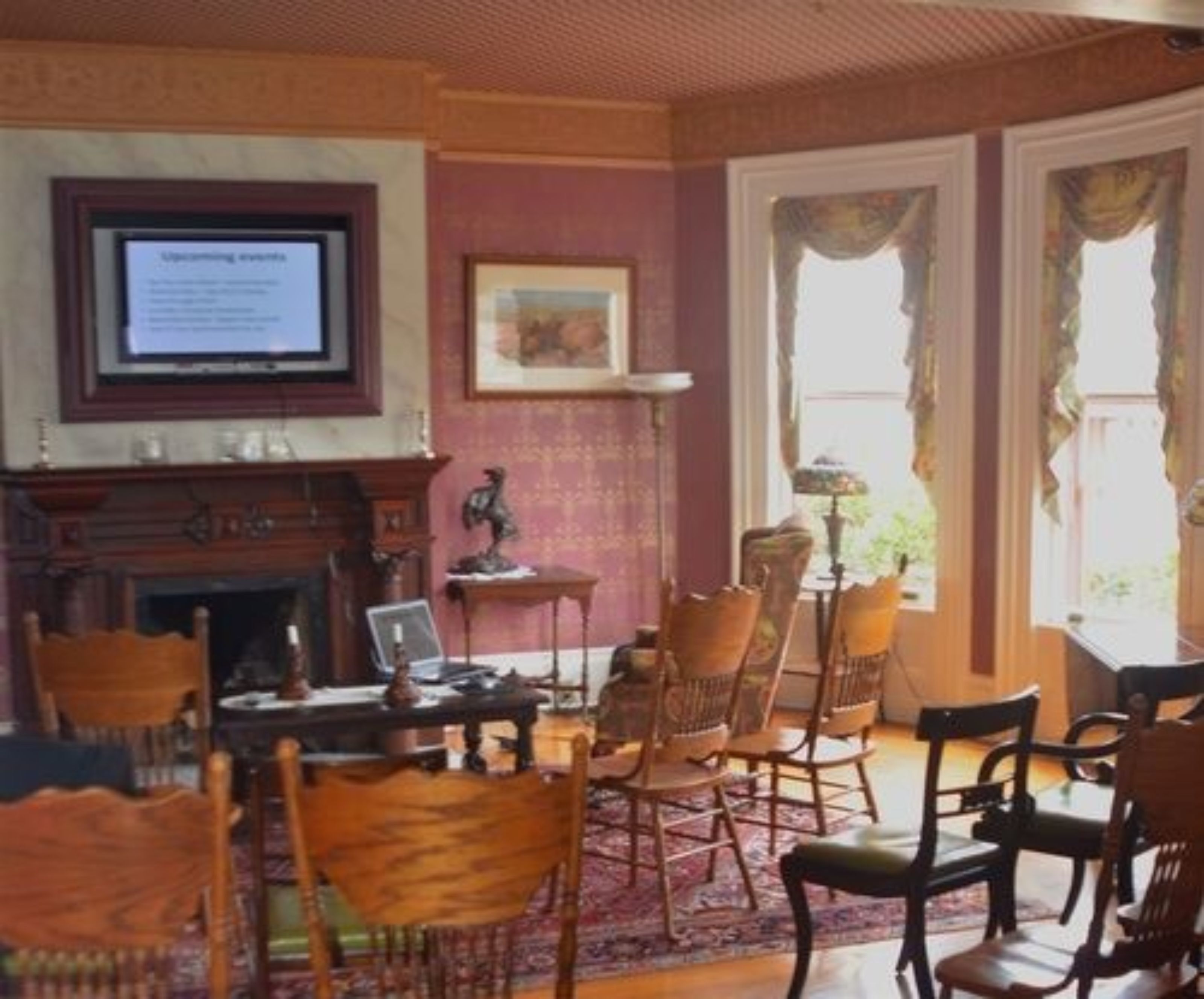 Una habitación tradicional con chimenea, varias sillas, una mesa y un televisor mostrando información.