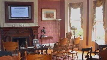 Una habitación tradicional con chimenea, varias sillas, una mesa y un televisor mostrando información.