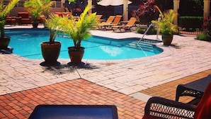 A pool area with lounge chairs, potted plants, and a large building with a clock.