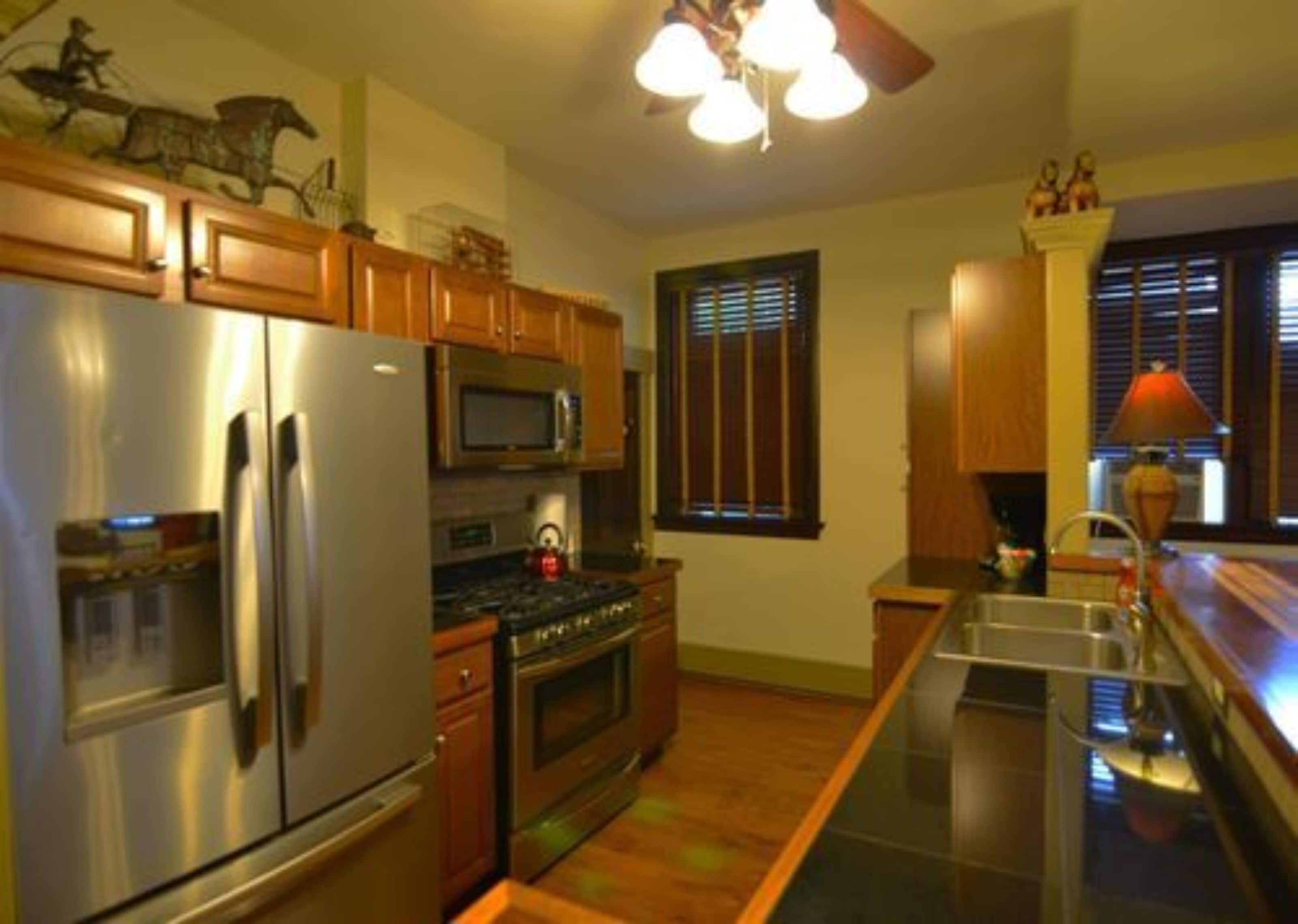 A kitchen with wooden cabinets, stainless steel appliances, a microwave, a stove, and a window with blinds.