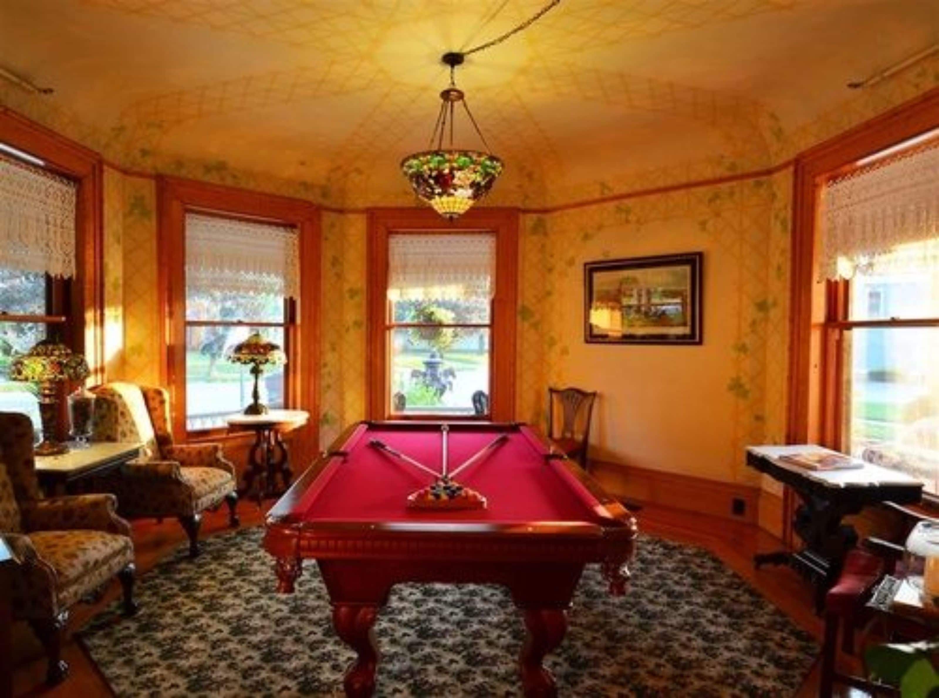 Une salle de billard équipée d’une table de billard, de chaises en bois et d’un lustre.