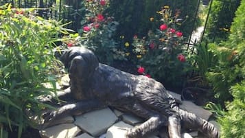 Una estatua de jardín de un perro acostado sobre una losa de piedra, rodeado de flores y follaje.
