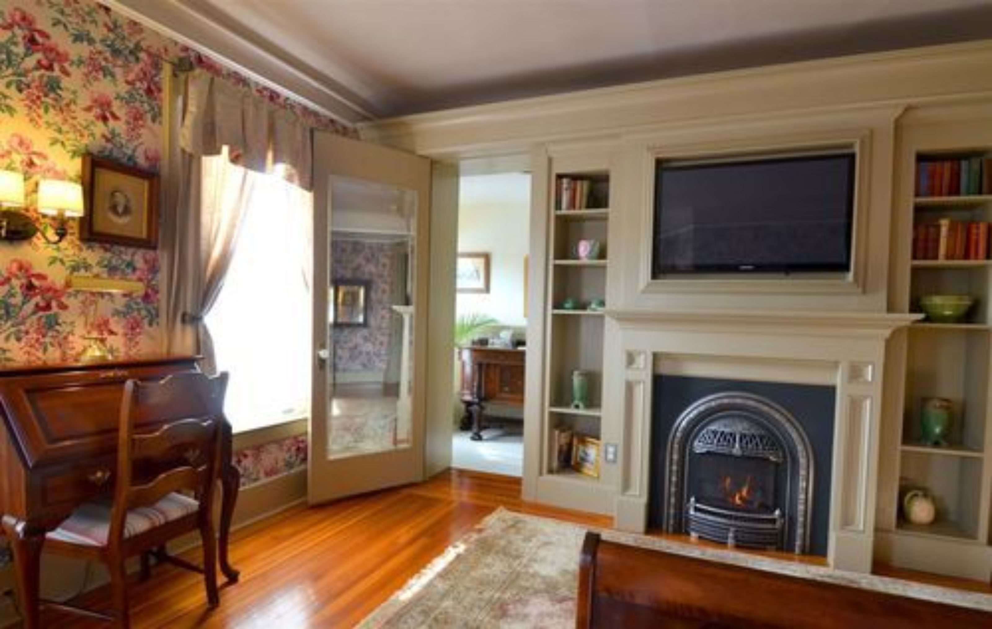 A living room with a fireplace, wooden flooring, a piano, and a bookshelf.