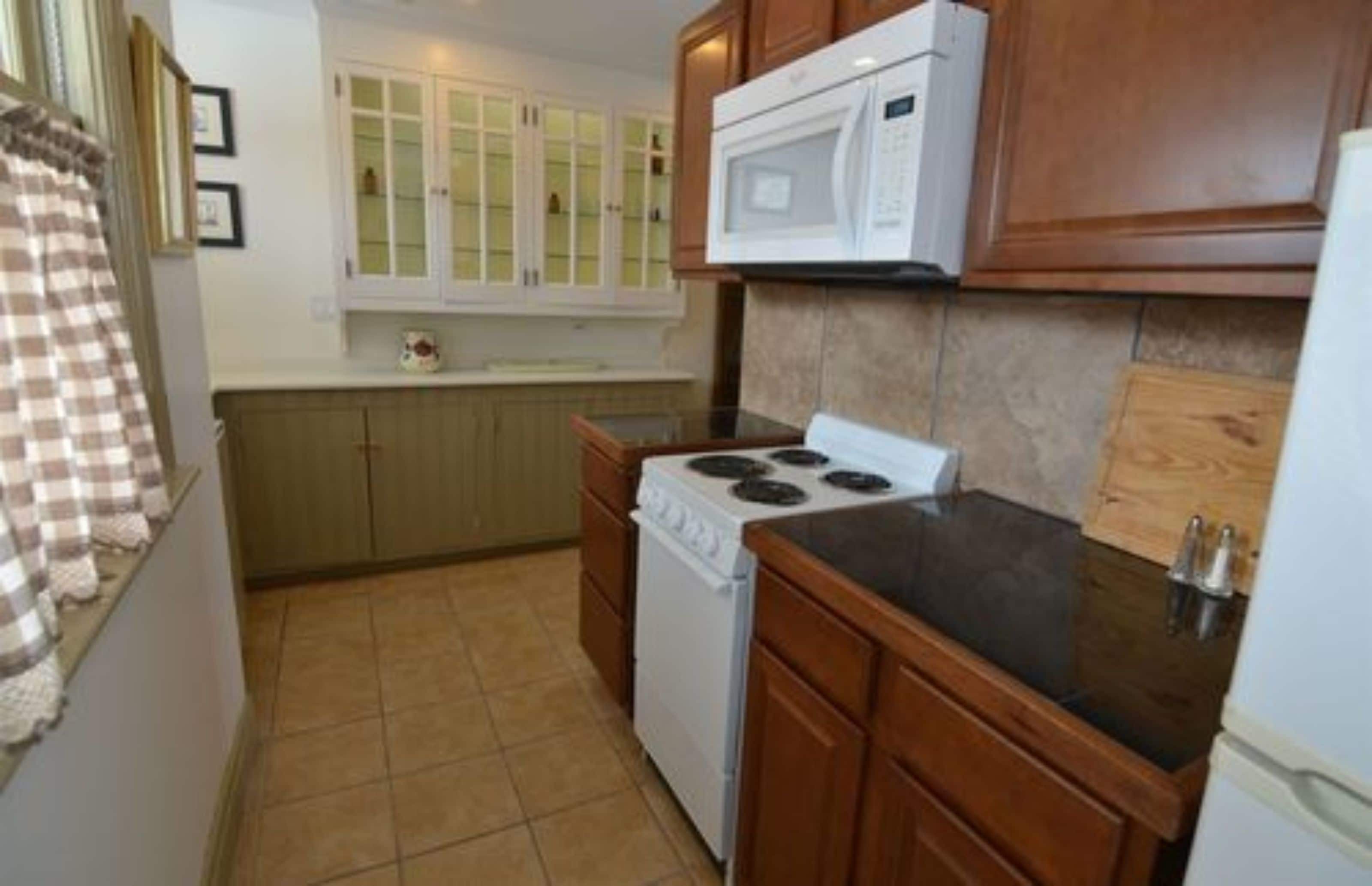 A compact kitchen with a stove, microwave, and wooden cabinets.