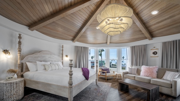 A spacious bedroom with a large bed, a wooden ceiling, a hanging light fixture, and a view of the outdoors. - Cardiff by the Sea Lodge (Cardiff-by-the-Sea)