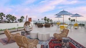 A rooftop terrace with wicker furniture, round tables, and striped umbrellas. - Cardiff by the Sea Lodge (Cardiff-by-the-Sea)