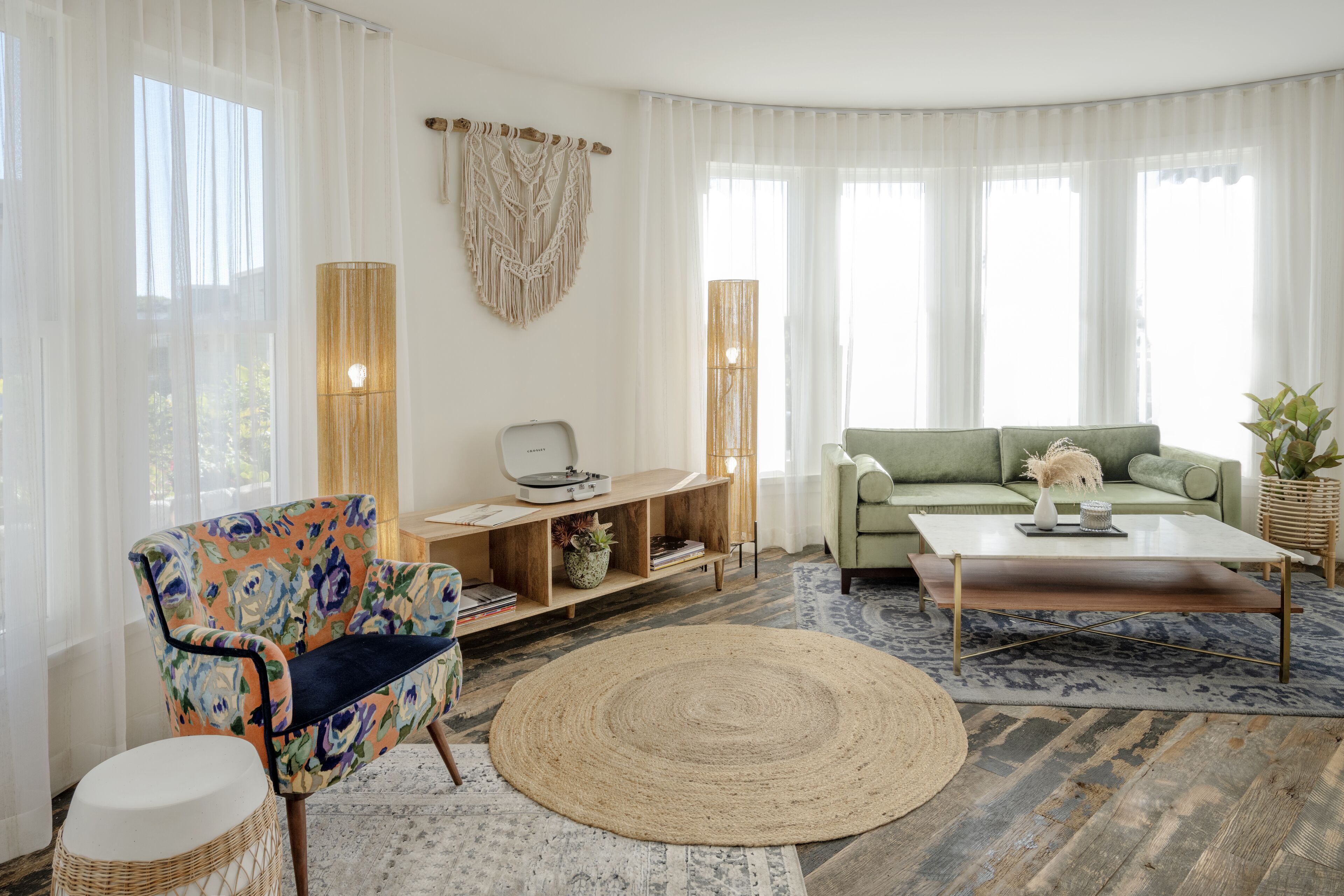 Una sala de estar con sofá, mesa de centro y un sillón. Se ve un aparador de madera con una planta y libros.