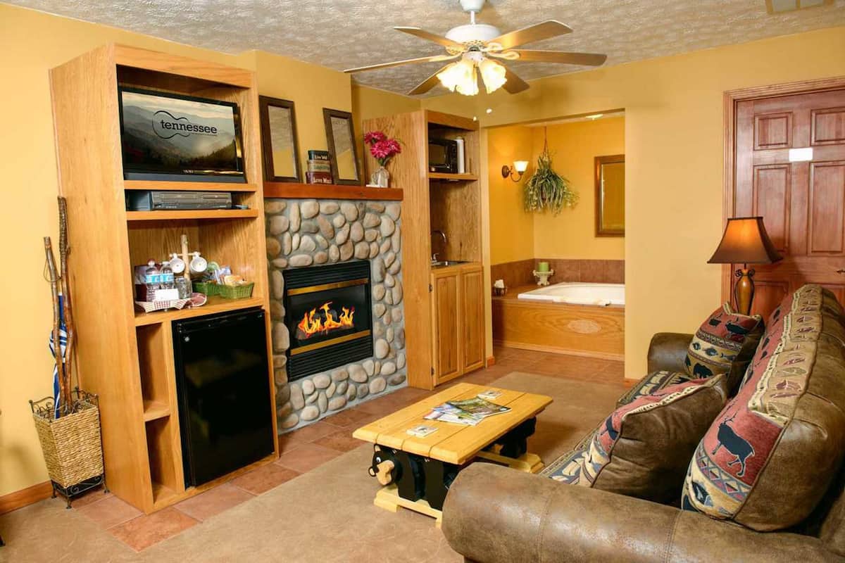 A cozy living room with a fireplace, a television, a ceiling fan, and a couch with patterned cushions.