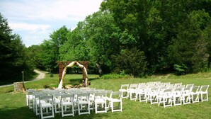 An outdoor wedding ceremony setup with white chairs arranged in rows and a wooden arch adorned with flowers. - Berry Springs Lodge (Sevierville)