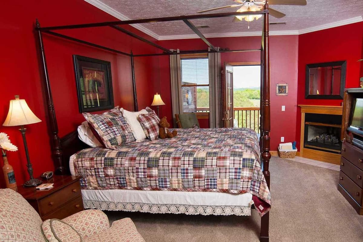 A bedroom with a four-poster bed, a fireplace, and a view of the outdoors.