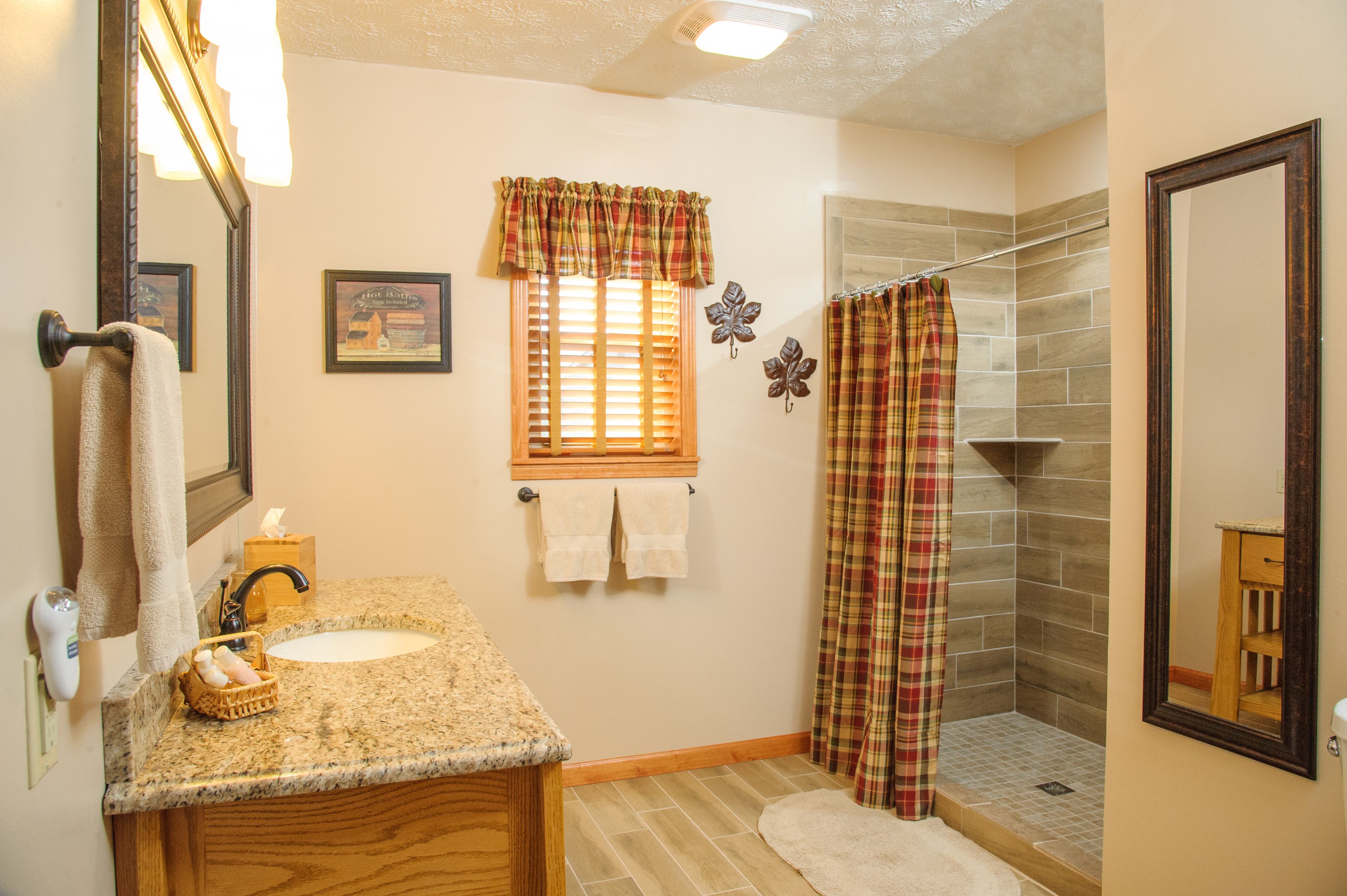 A bathroom with a granite countertop sink, a wooden vanity, a shower with a plaid curtain, and a mirror.