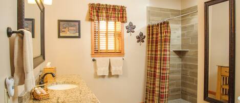 A bathroom with a granite countertop sink, a wooden vanity, a shower with a plaid curtain, and a mirror.