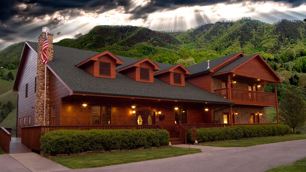 A large log cabin with a stone chimney, multiple windows, and a balcony.