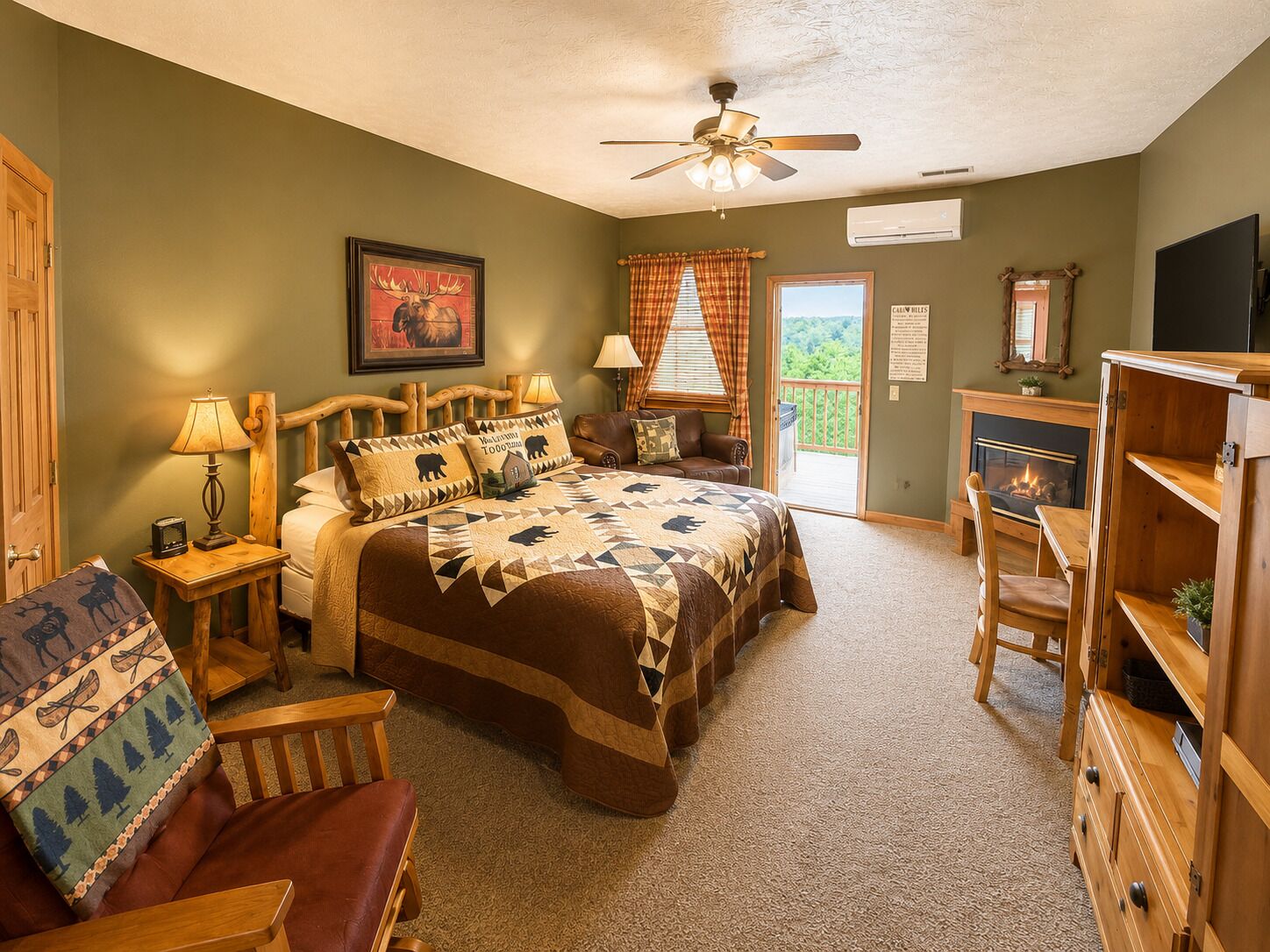 A bedroom with a large bed, a wooden headboard, a ceiling fan, a fireplace, a television, and a view of the outdoors through a sliding door.