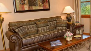 A brown leather sofa with patterned cushions, a wooden coffee table with a book and a basket, and a framed abstract painting above. - Berry Springs Lodge (Sevierville)