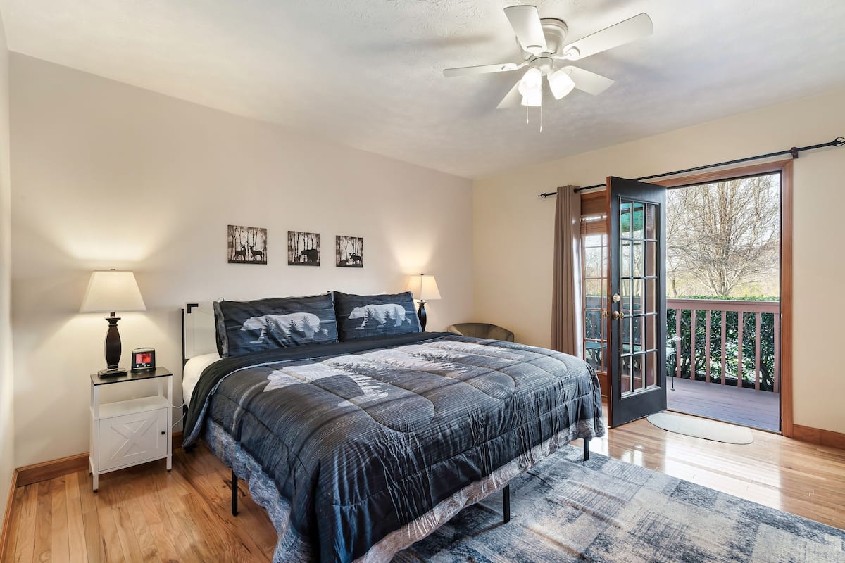 A bedroom with a bed, nightstands, a ceiling fan, and a view of the outdoors through a door.