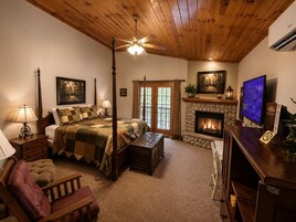 A four-poster bed with a quilt, a fireplace, a television, and a desk with a computer.