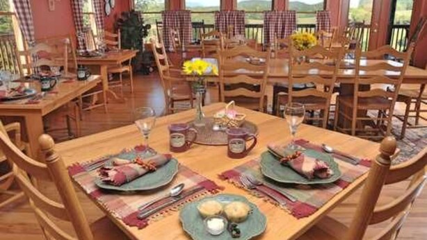 A dining area with wooden tables and chairs, set with plates, cutlery, and a vase of yellow flowers. - Berry Springs Lodge (Sevierville)