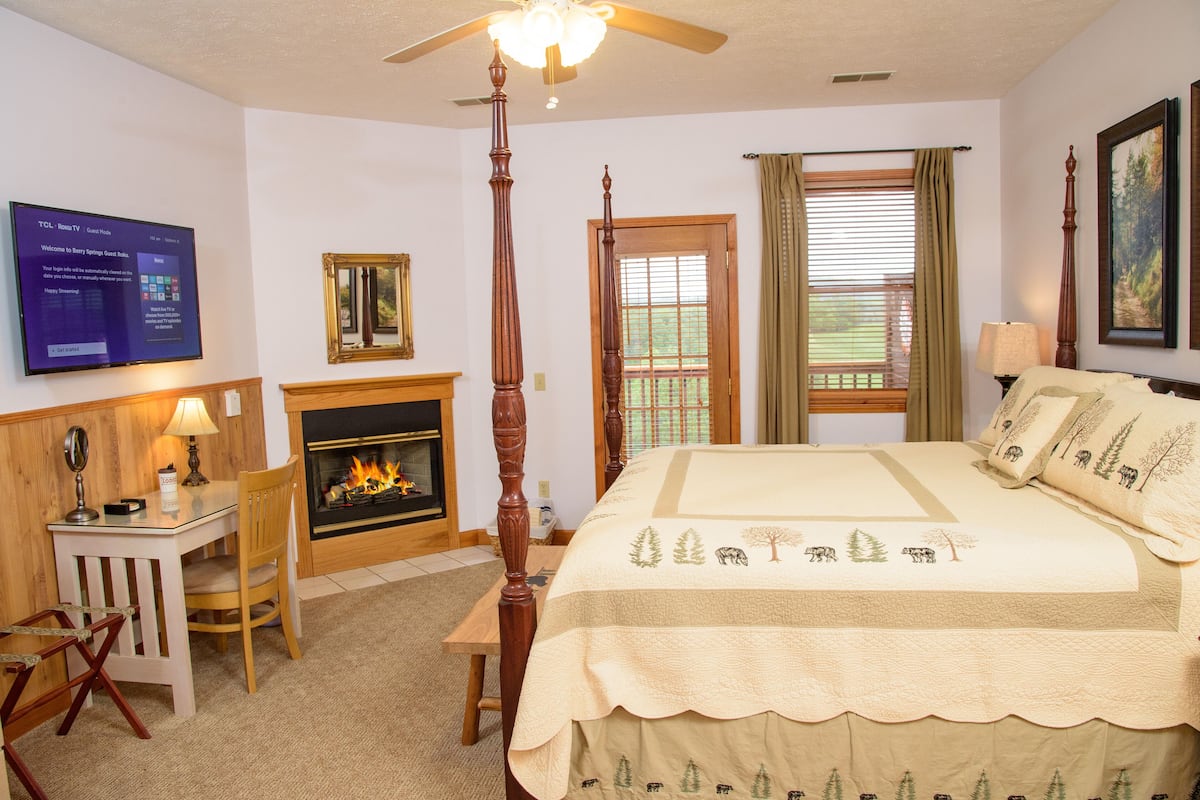 A hotel room with a four-poster bed, a fireplace, a television, and a window with curtains.
