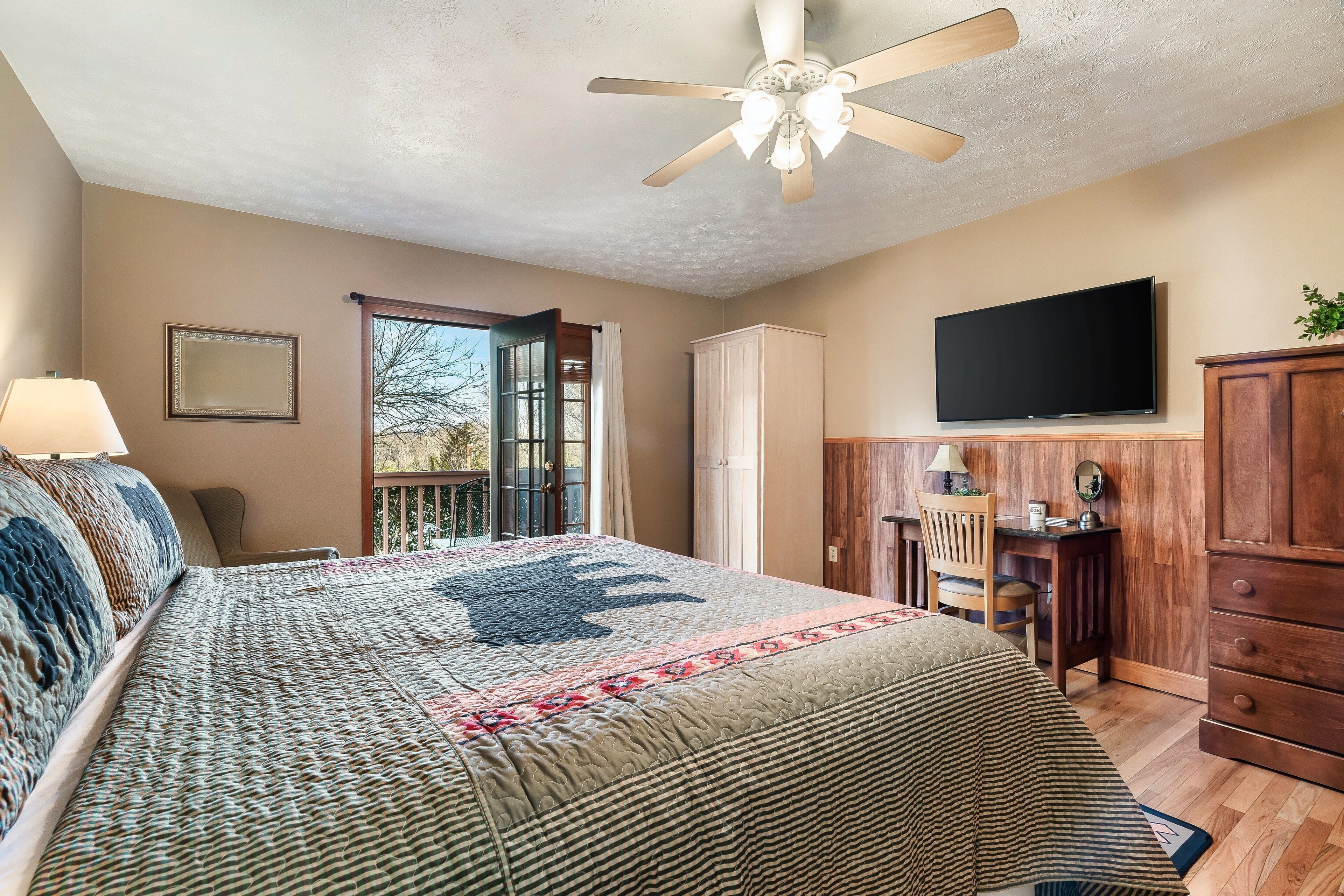 Ein Schlafzimmer mit Bett, Deckenventilator, Fernseher, Schreibtisch und Kleiderschrank.