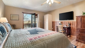 A bedroom with a bed, a ceiling fan, a TV, a desk, and a wardrobe.