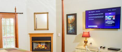 A room with a fireplace, a bed with a quilt, a desk with a lamp, and a TV displaying a menu.