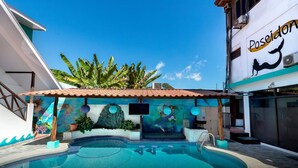 A swimming pool with a mural, a tiled roof, and a building with a Poseidon sign. - Hotel Trident Poseidon (Jacó)