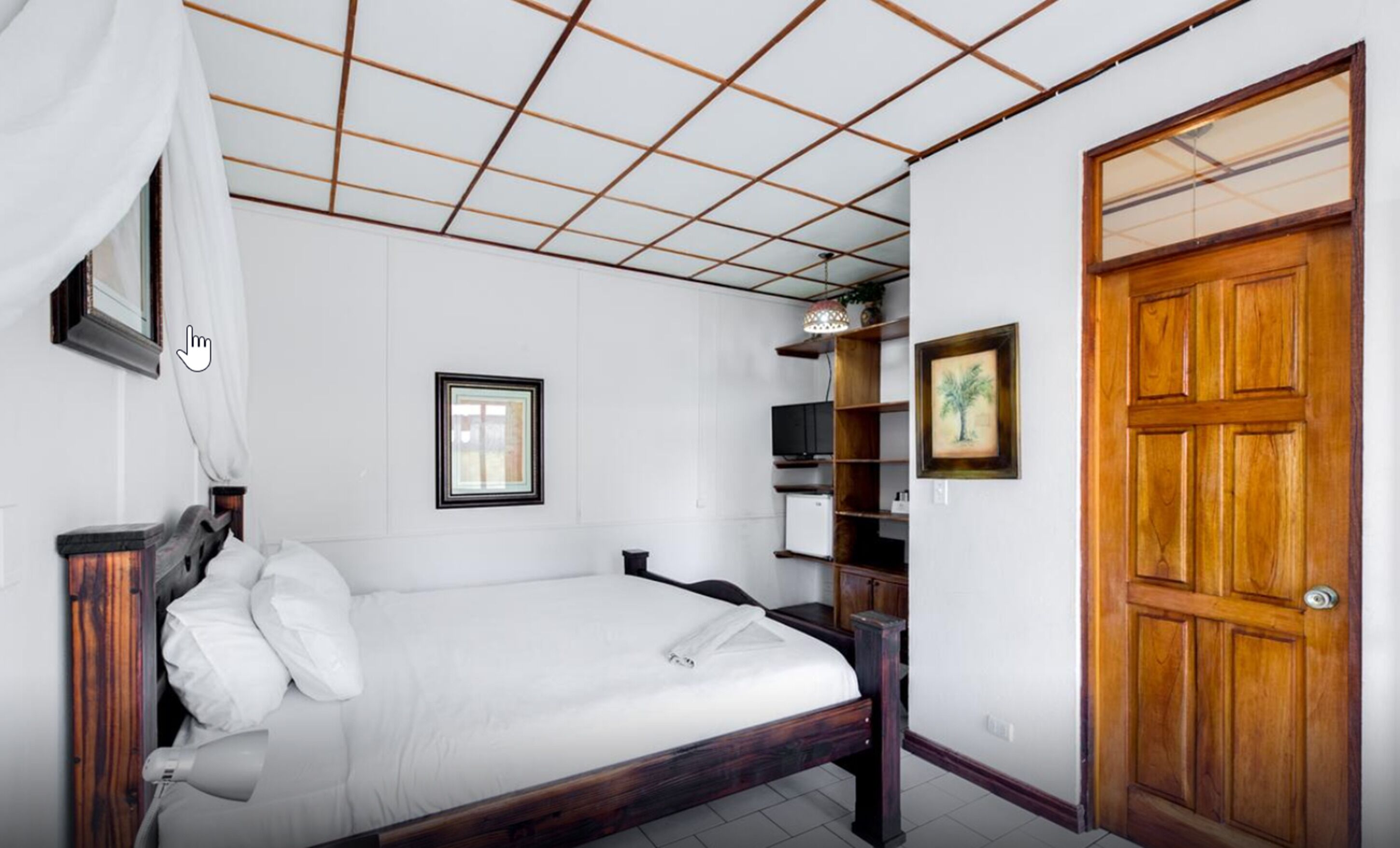 Une chambre avec un lit en bois, une petite fenêtre, une porte en bois et une étagère sur laquelle se trouve un téléviseur.