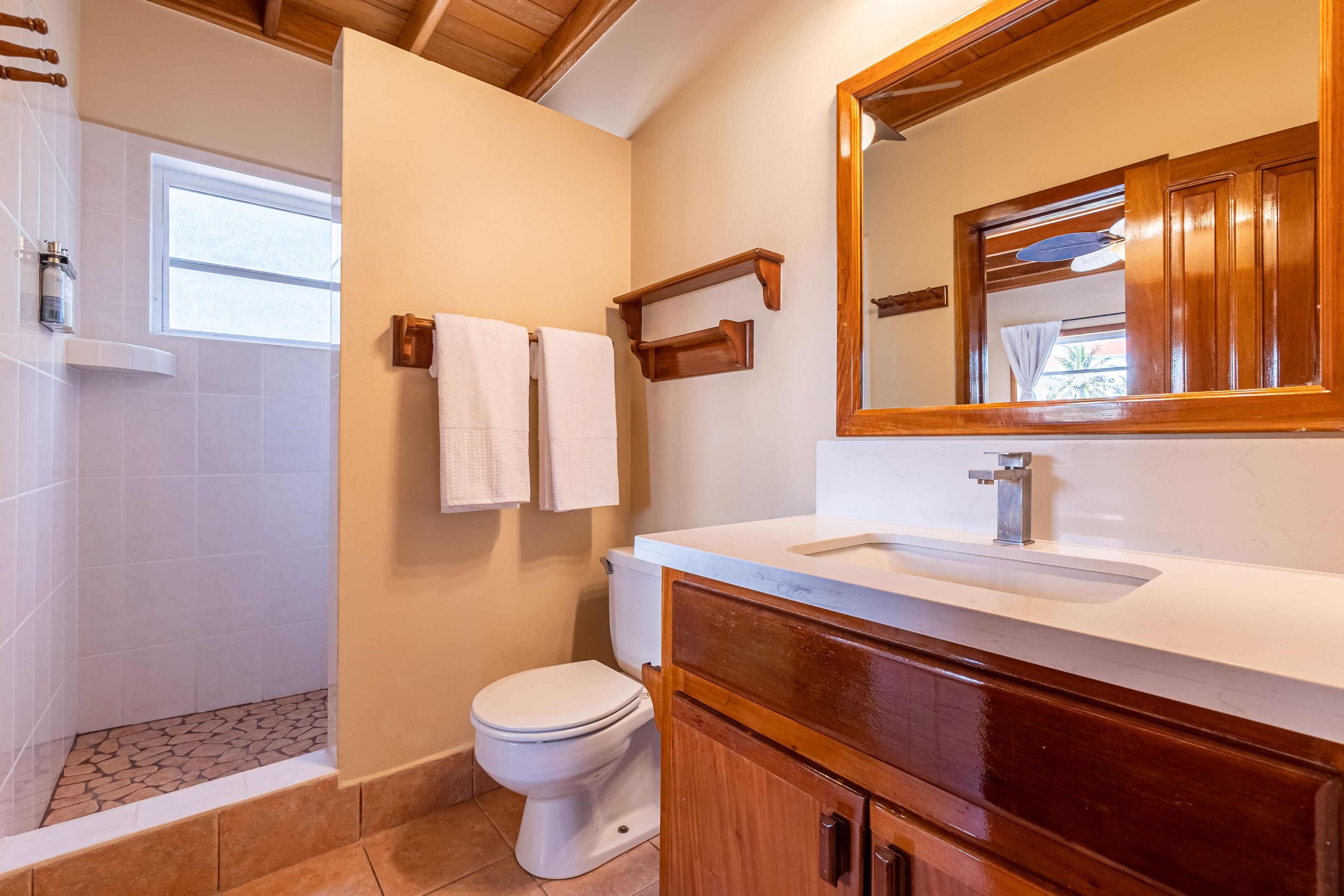A bathroom with a shower, toilet, vanity with a mirror, and a window.