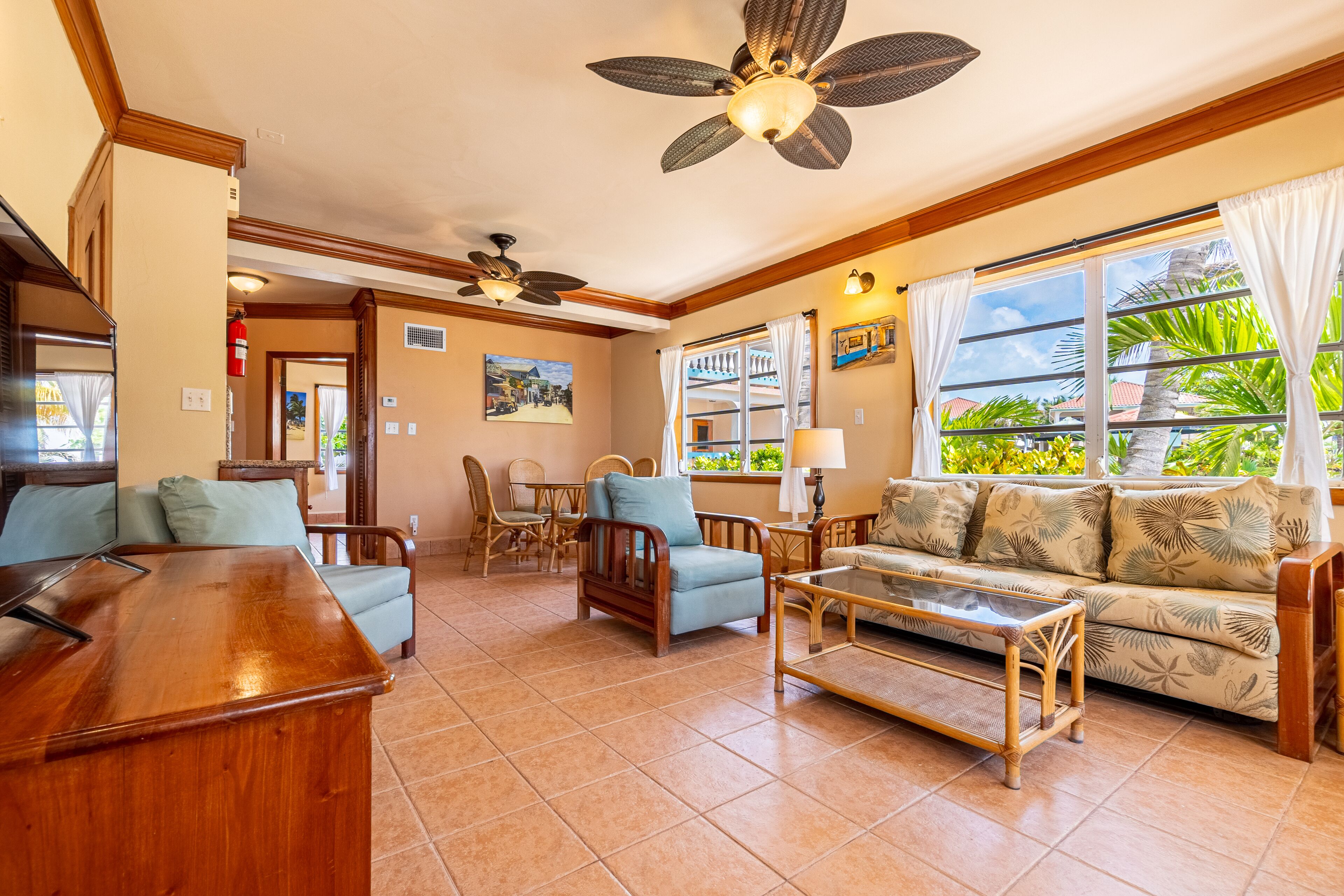 A living room with a wooden coffee table, blue armchairs, a sofa with tropical print, and a ceiling fan.