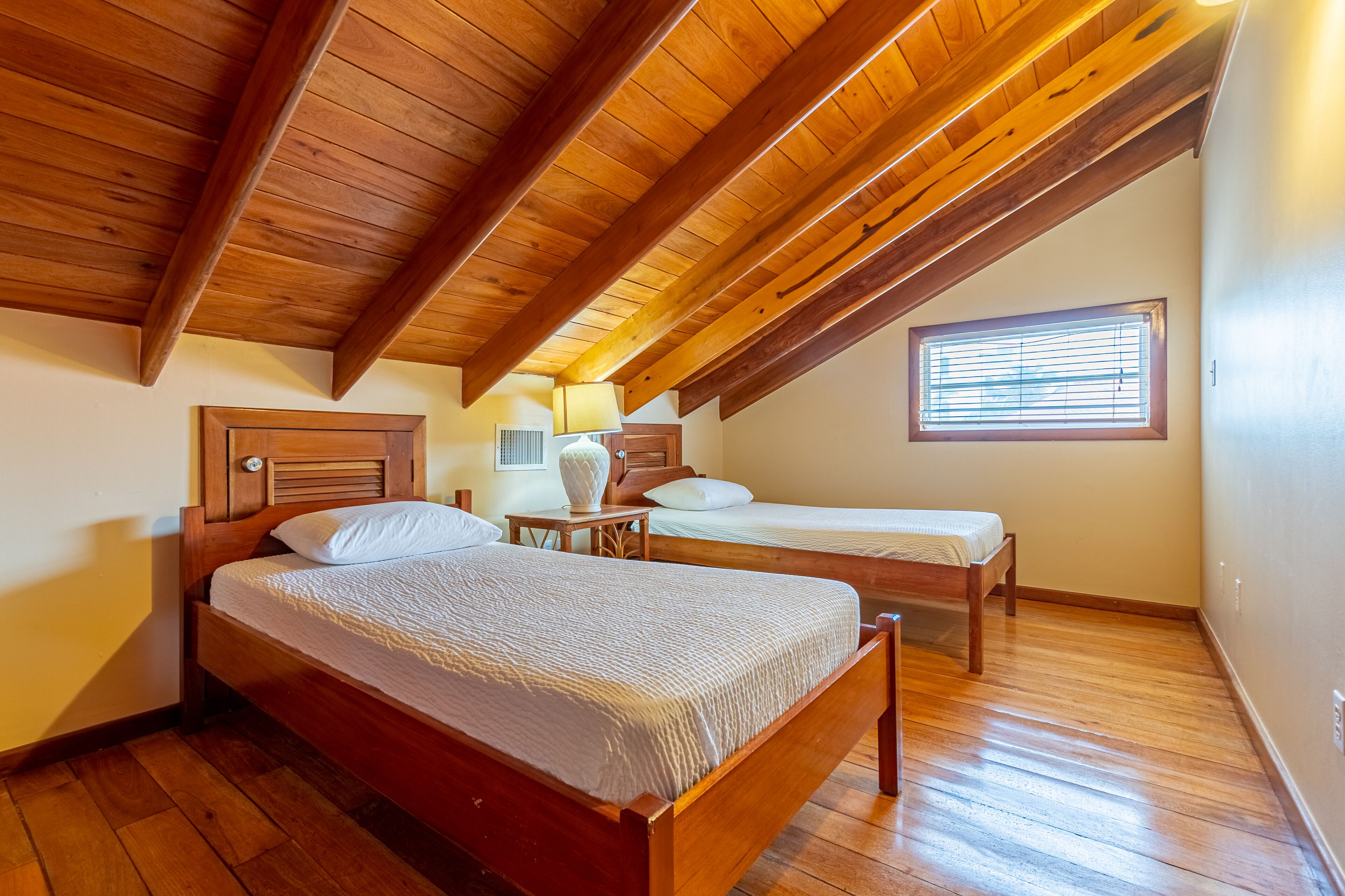 Una stanza con due letti di legno, una finestra con persiane e un soffitto in legno.