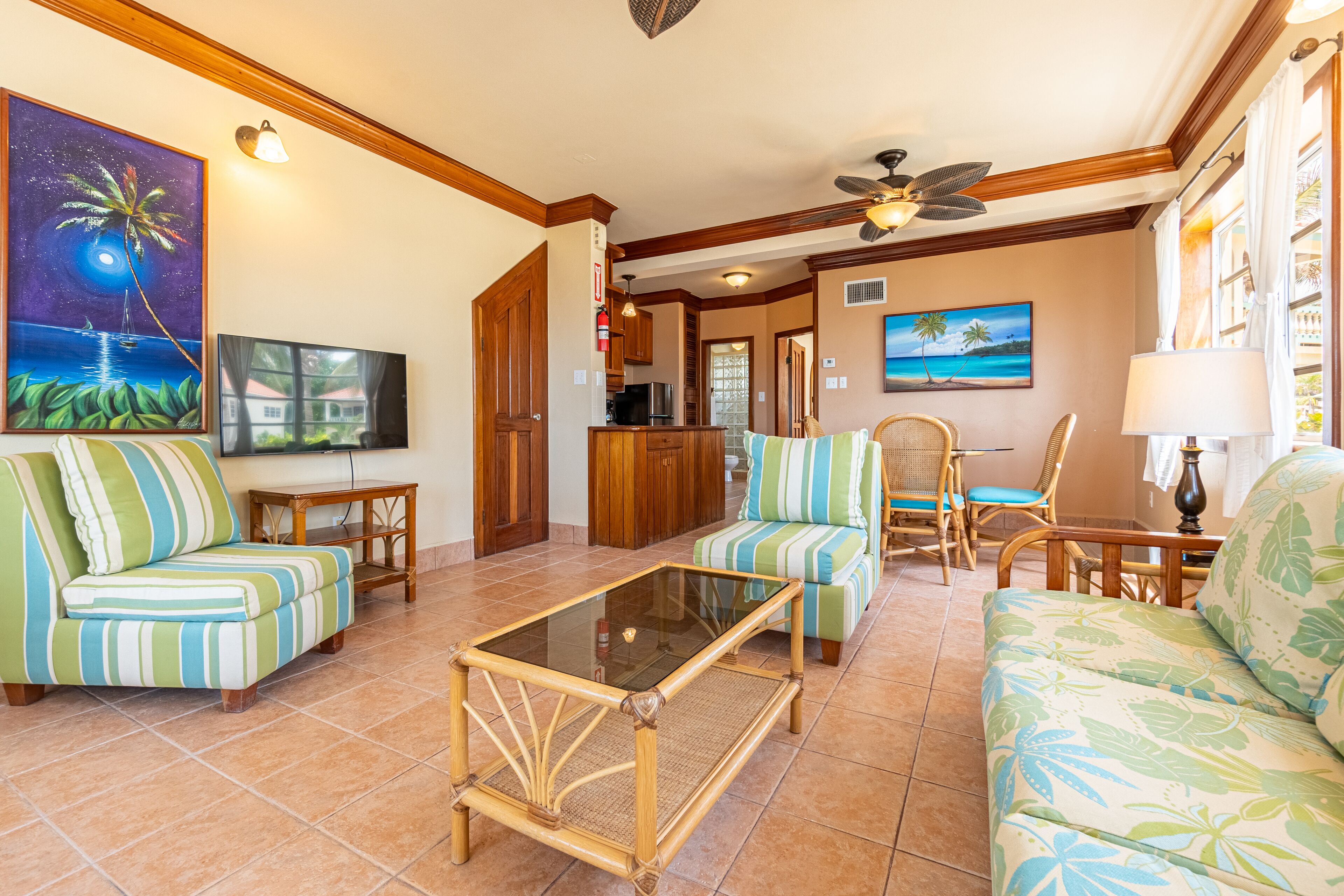 A spacious living room with a glass coffee table, striped sofas, and a television.