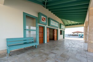 Un espacio al aire libre techado con una banca, puertas de madera y vista al mar.