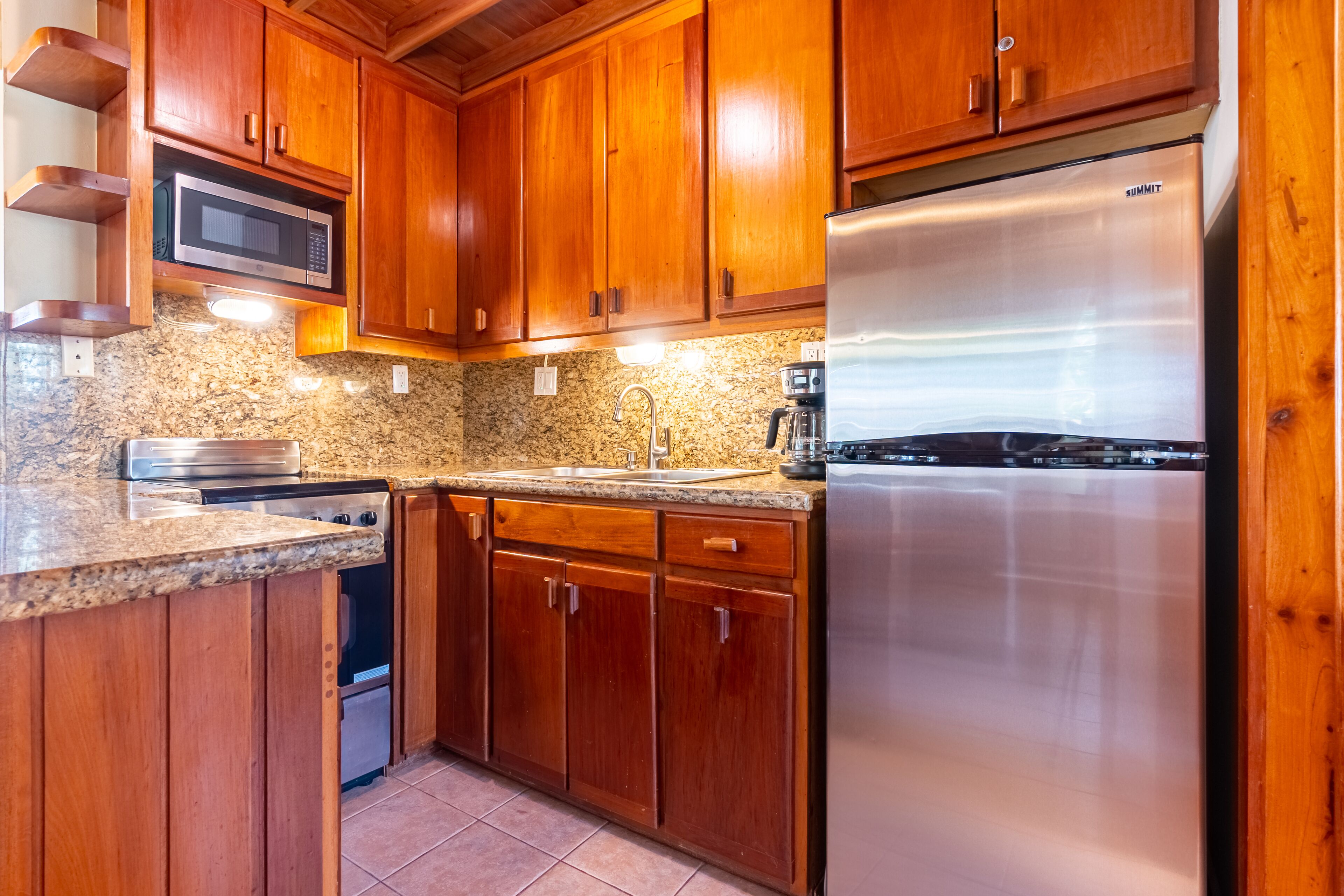 A kitchen with wooden cabinets, a stainless steel refrigerator, a microwave, and granite countertops.