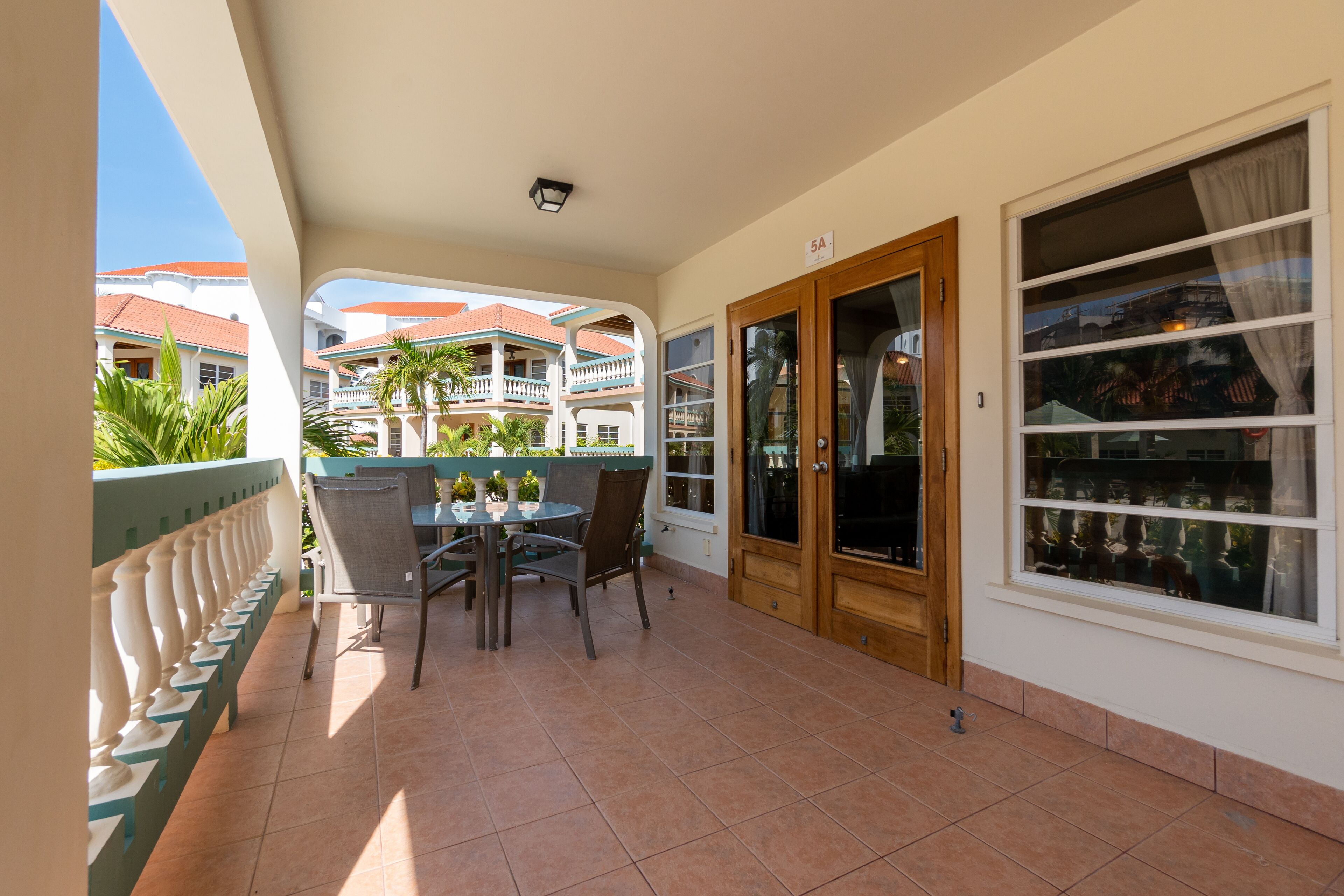 Un balcon avec une table et des chaises pour prendre les repas, une vue sur un immeuble aux toits rouges et une fenêtre avec des rideaux.