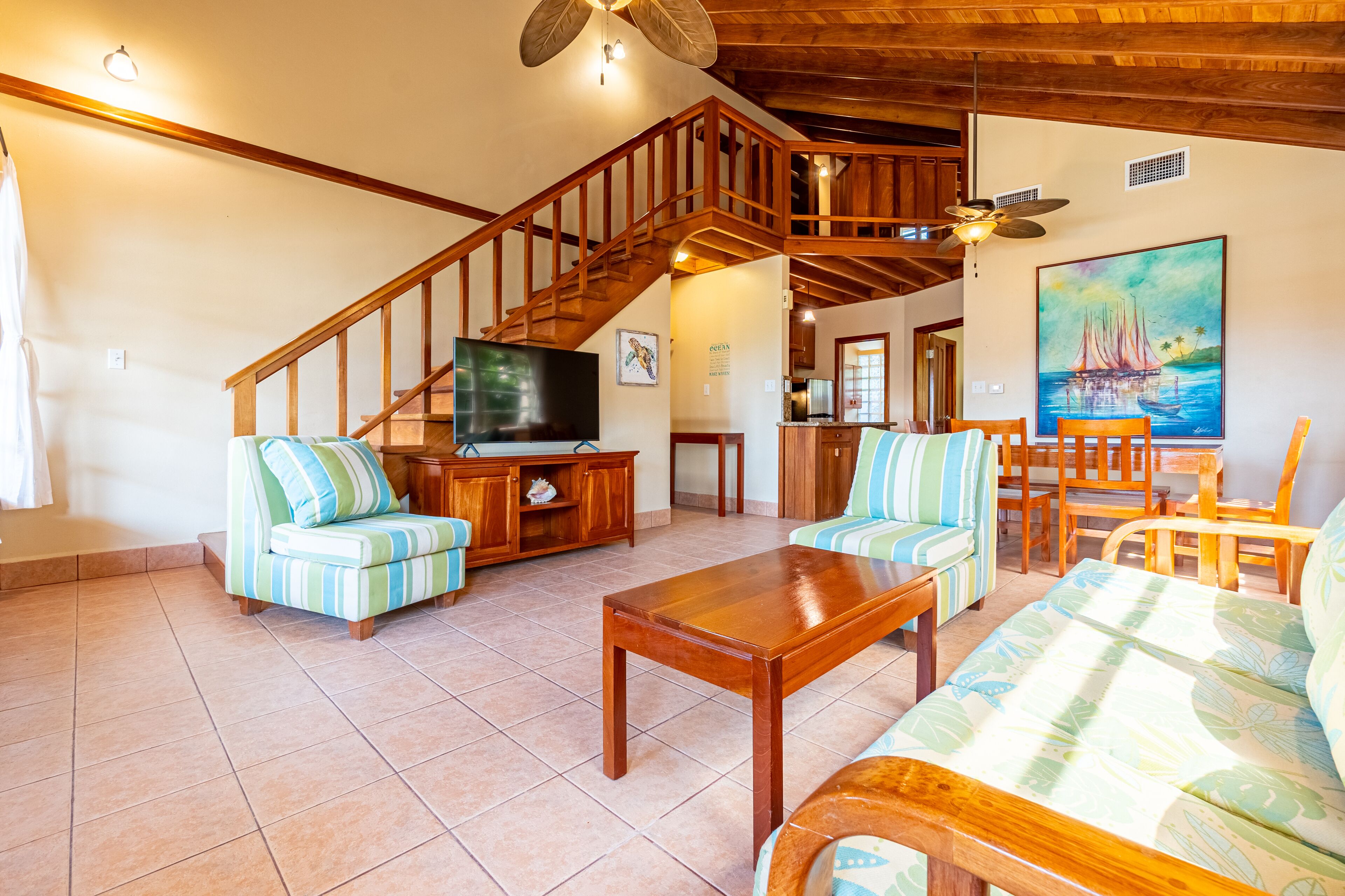 A spacious living room with a wooden staircase, a television, and a painting of a sailboat.