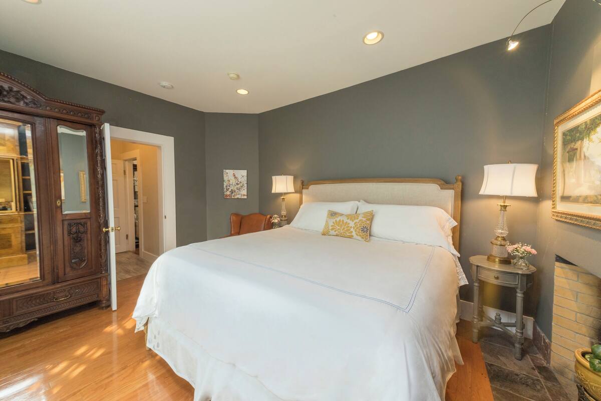 A bedroom with a large bed, two bedside tables with lamps, a wooden wardrobe, and a painting on the wall.