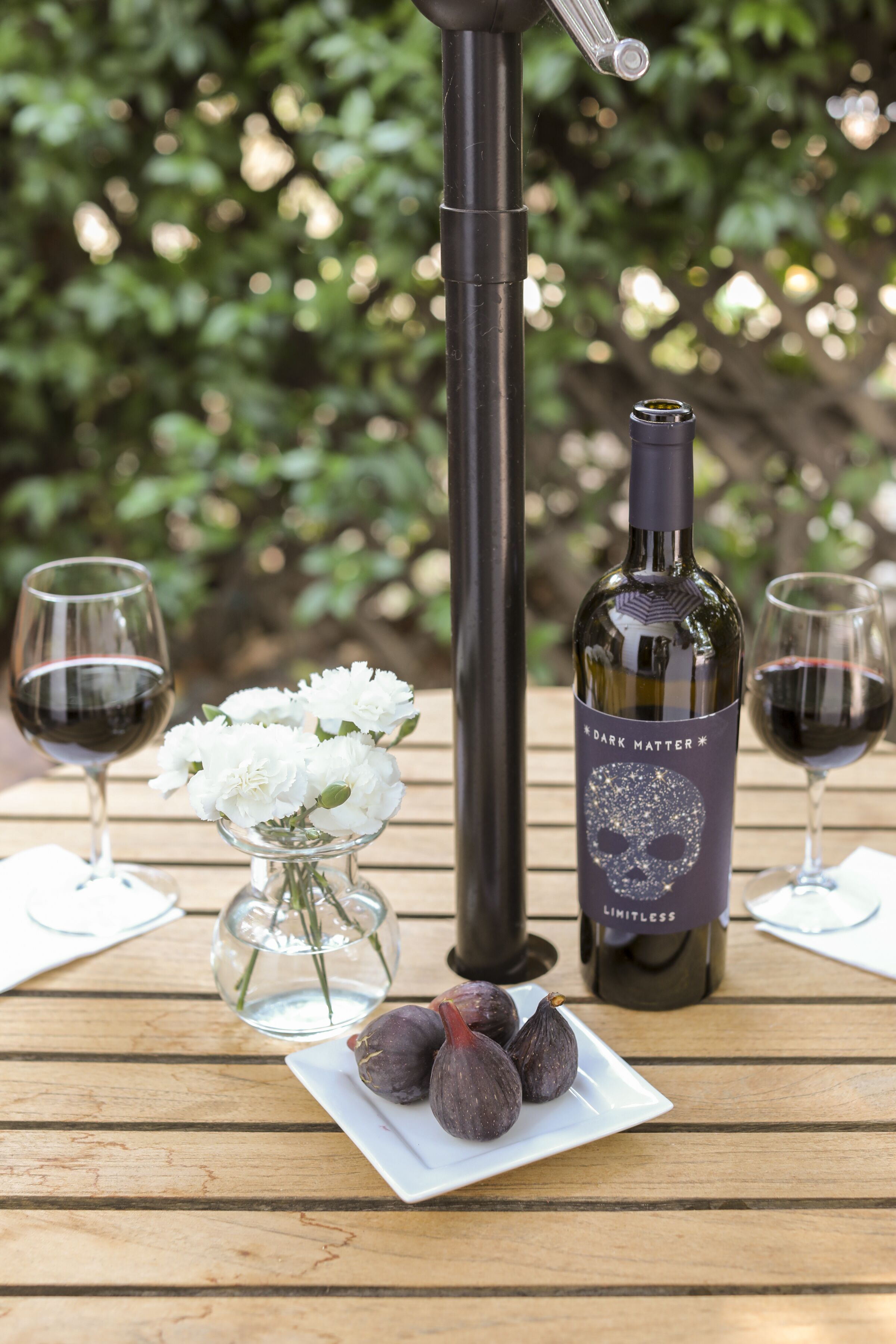 A bottle of wine, two glasses, and a plate with figs on a wooden table.