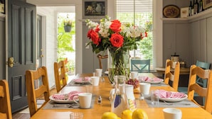 A dining room with a wooden table set for six, featuring a centerpiece of lemons and flowers, chairs, and a ceiling fan. - Inn St Helena (St. Helena)